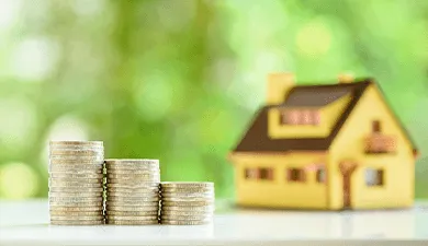 A yellow and brown house with coins stacked in front of it