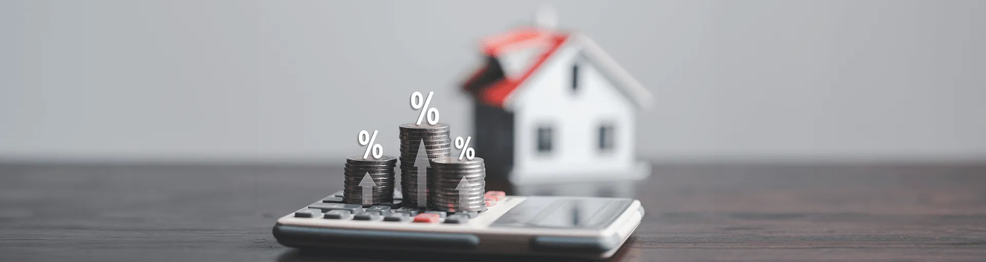 A house in the background and a calculator with coins stacked atop it
